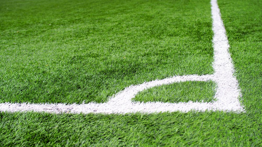 Close-up of a soccer field's corner, showing bright green grass and crisp white lines defining the right-angle boundary area.