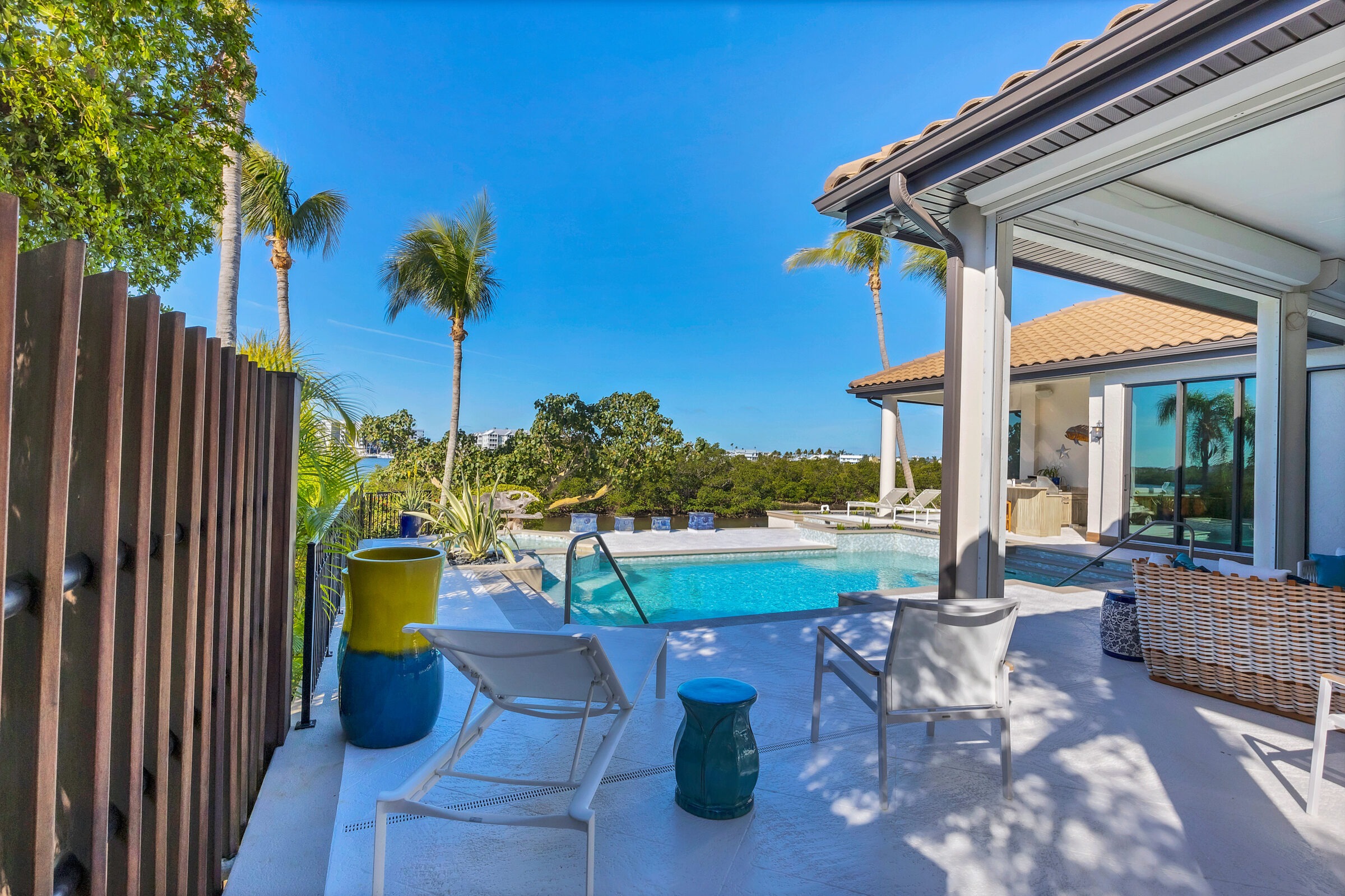 A luxurious poolside view features tropical landscaping, modern furniture, and a clear blue sky, evoking a serene and upscale atmosphere.