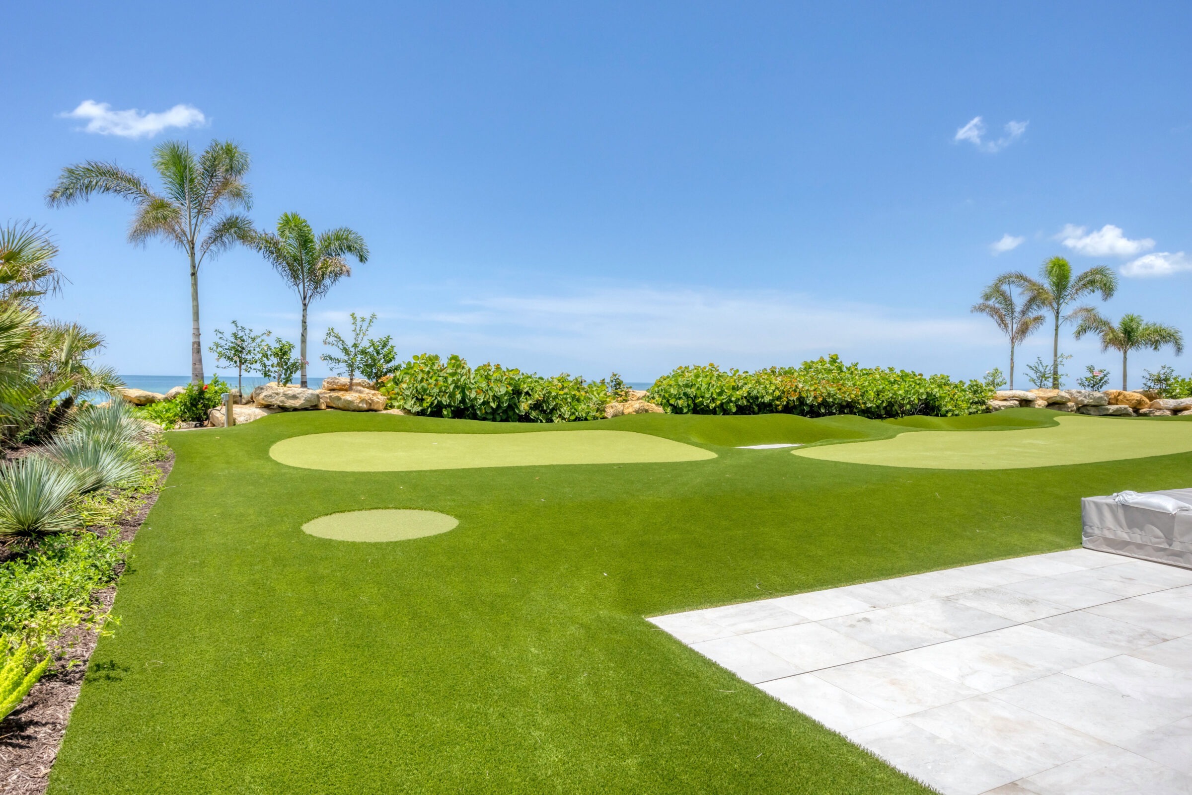 Lush green lawn with putting green, palm trees, and ocean view under clear blue sky. Peaceful and scenic outdoor setting perfect for relaxation.