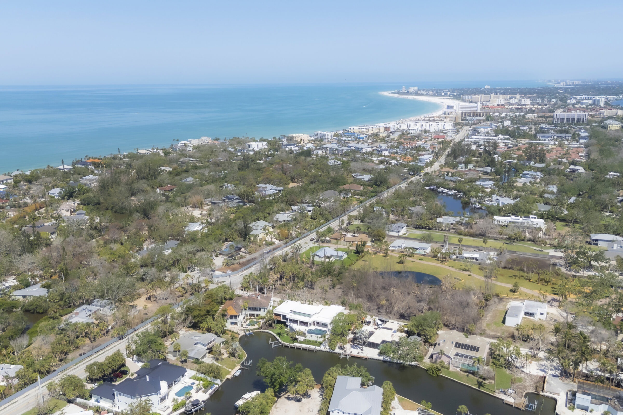 Coastal aerial view with a beach, residential area, ocean, and surrounding greenery, capturing a serene blend of city infrastructure and natural beauty.