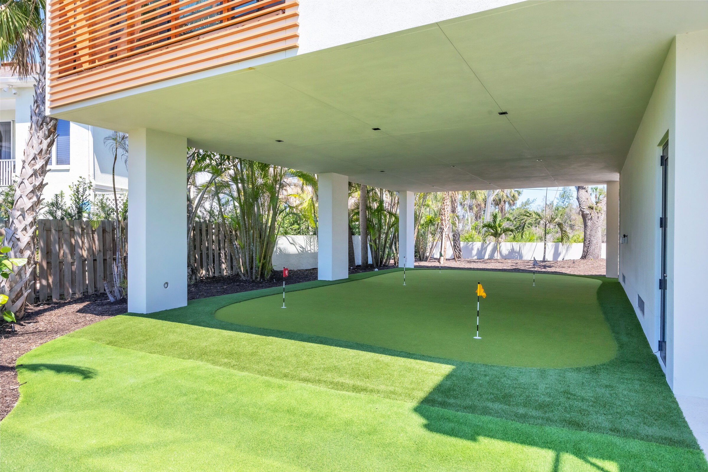 A covered outdoor area with a mini-golf putting green, surrounded by tropical plants and modern architectural elements.