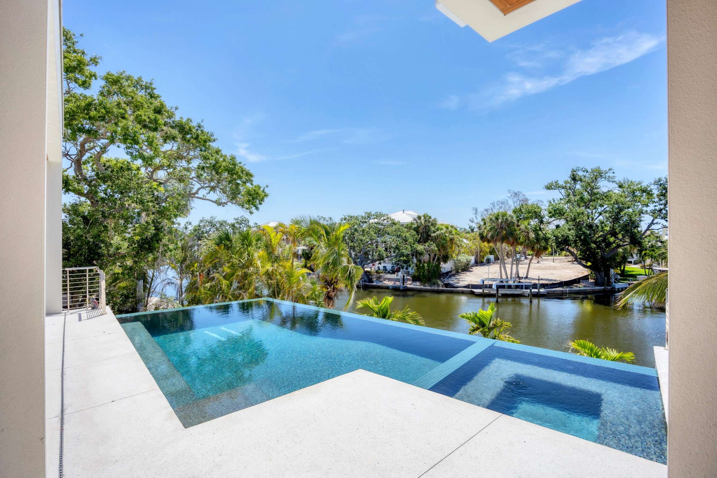 Infinity pool overlooking a serene waterway surrounded by lush greenery and palm trees, under a clear blue sky.