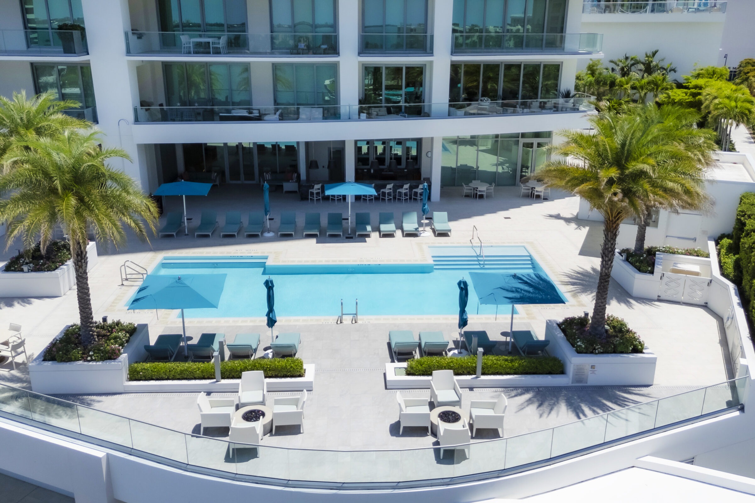 Modern hotel with clear swimming pool, lounge chairs, and umbrellas surrounded by palm trees and greenery, creating a relaxing outdoor atmosphere.