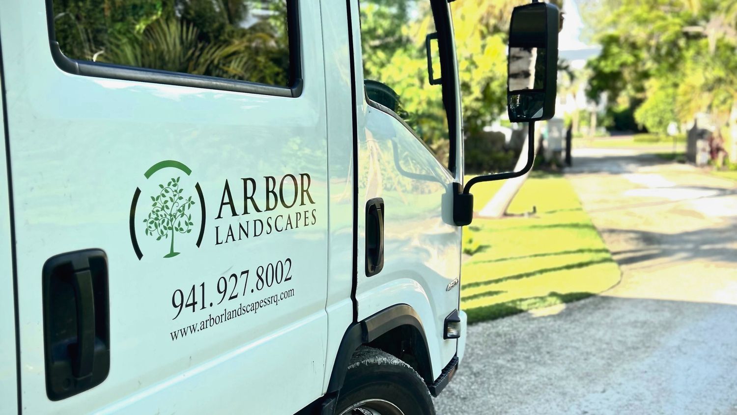 A truck from Arbor Landscapes parked on a sunny, tree-lined street, showcasing its logo and contact information.