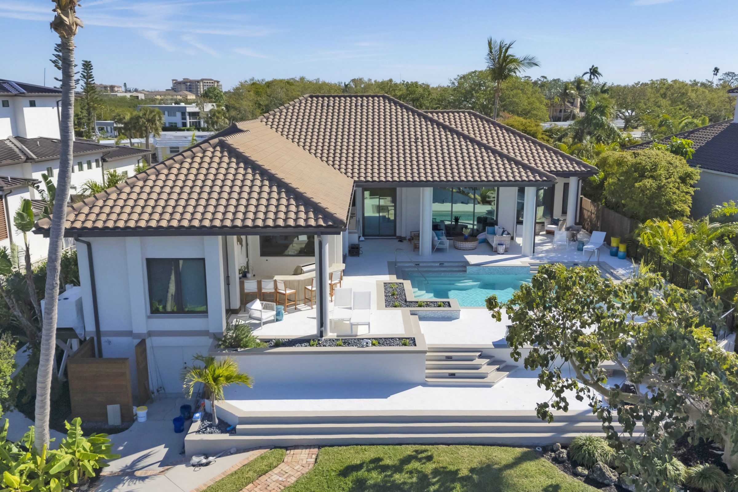 Modern villa with terracotta roof, large pool, lush landscaping, and private dock with colorful kayaks.