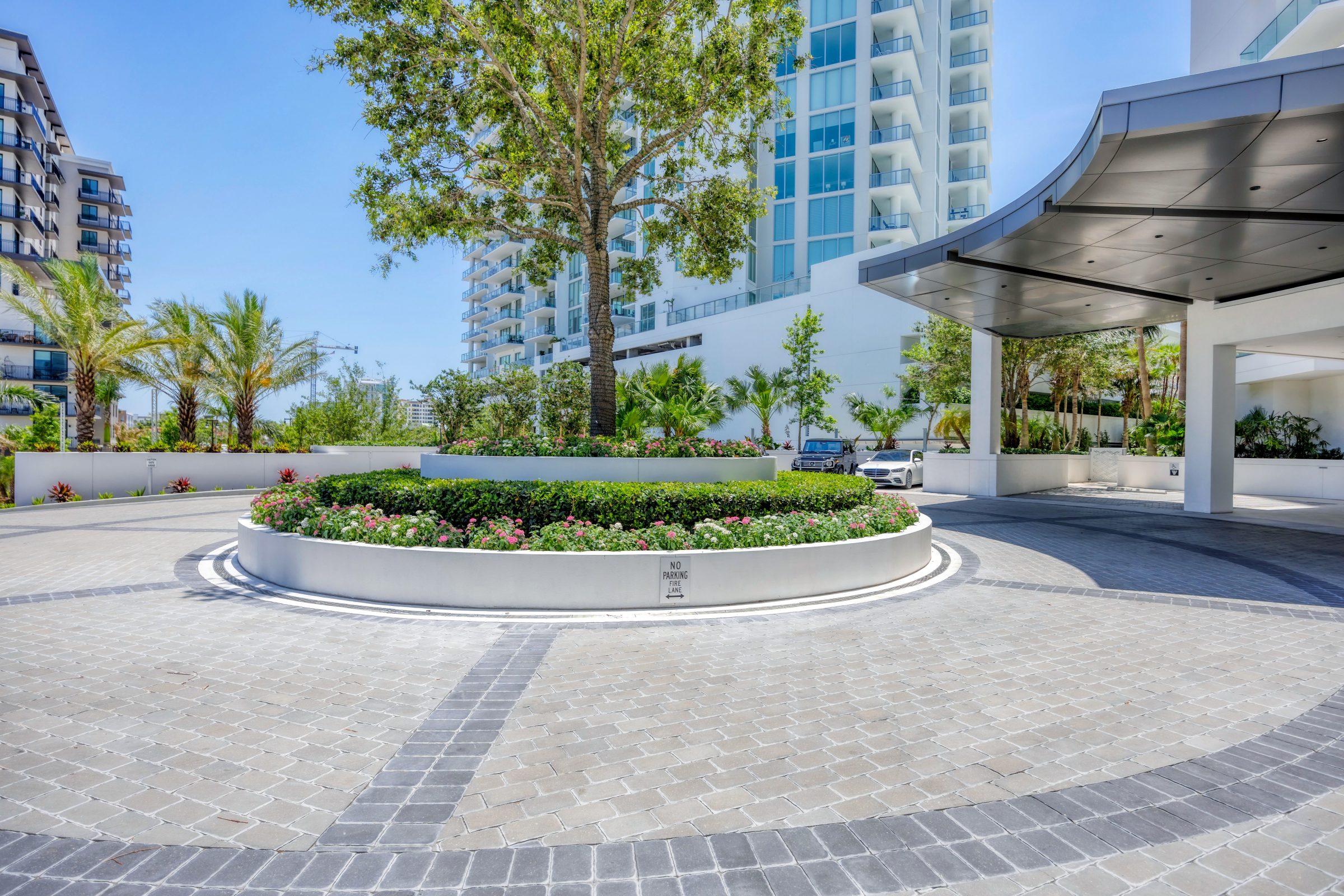 Circular driveway with a landscaped center island featuring a tree and flowers.