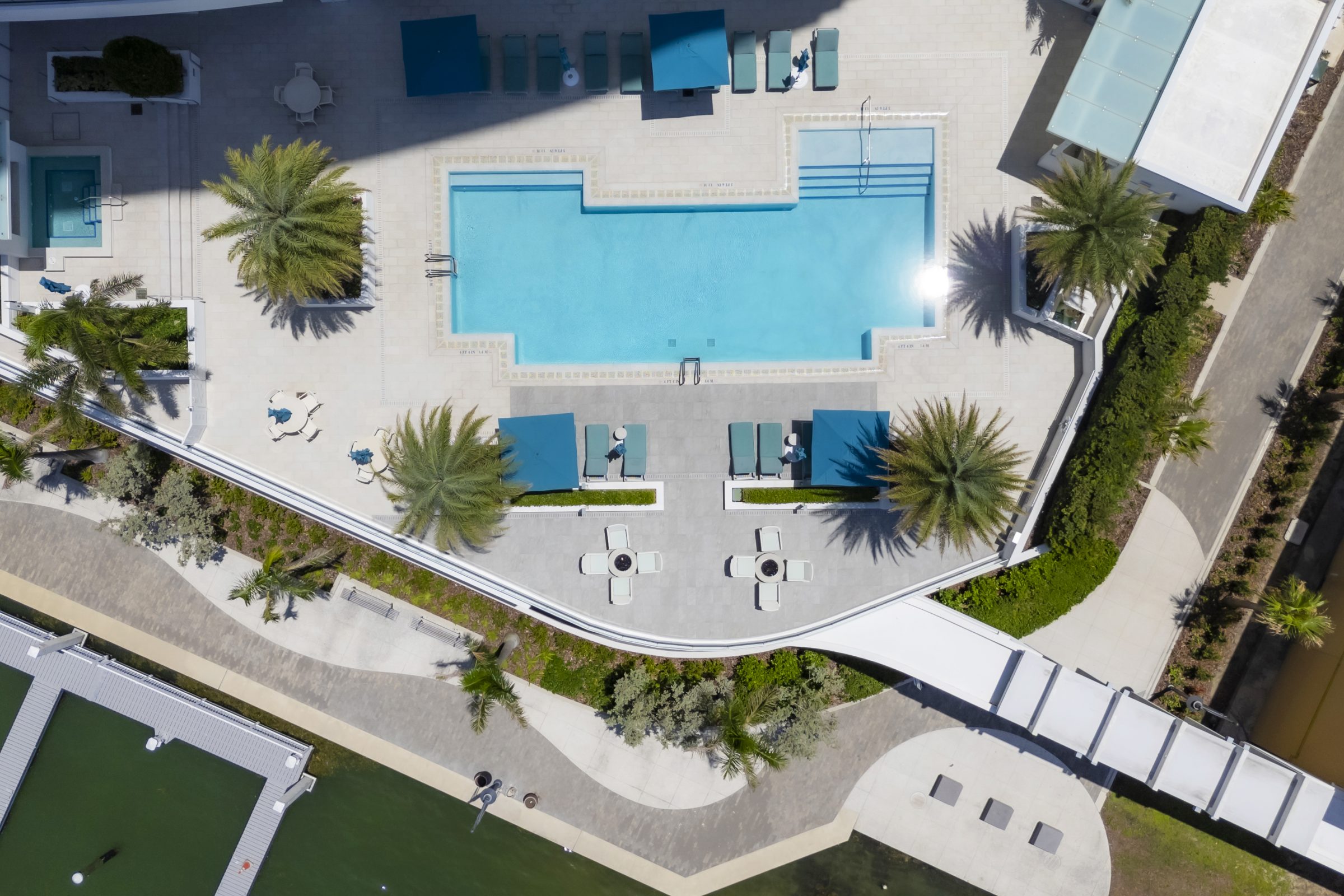 Overhead shot of a large rectangular pool with loungers, umbrellas, and palm trees.